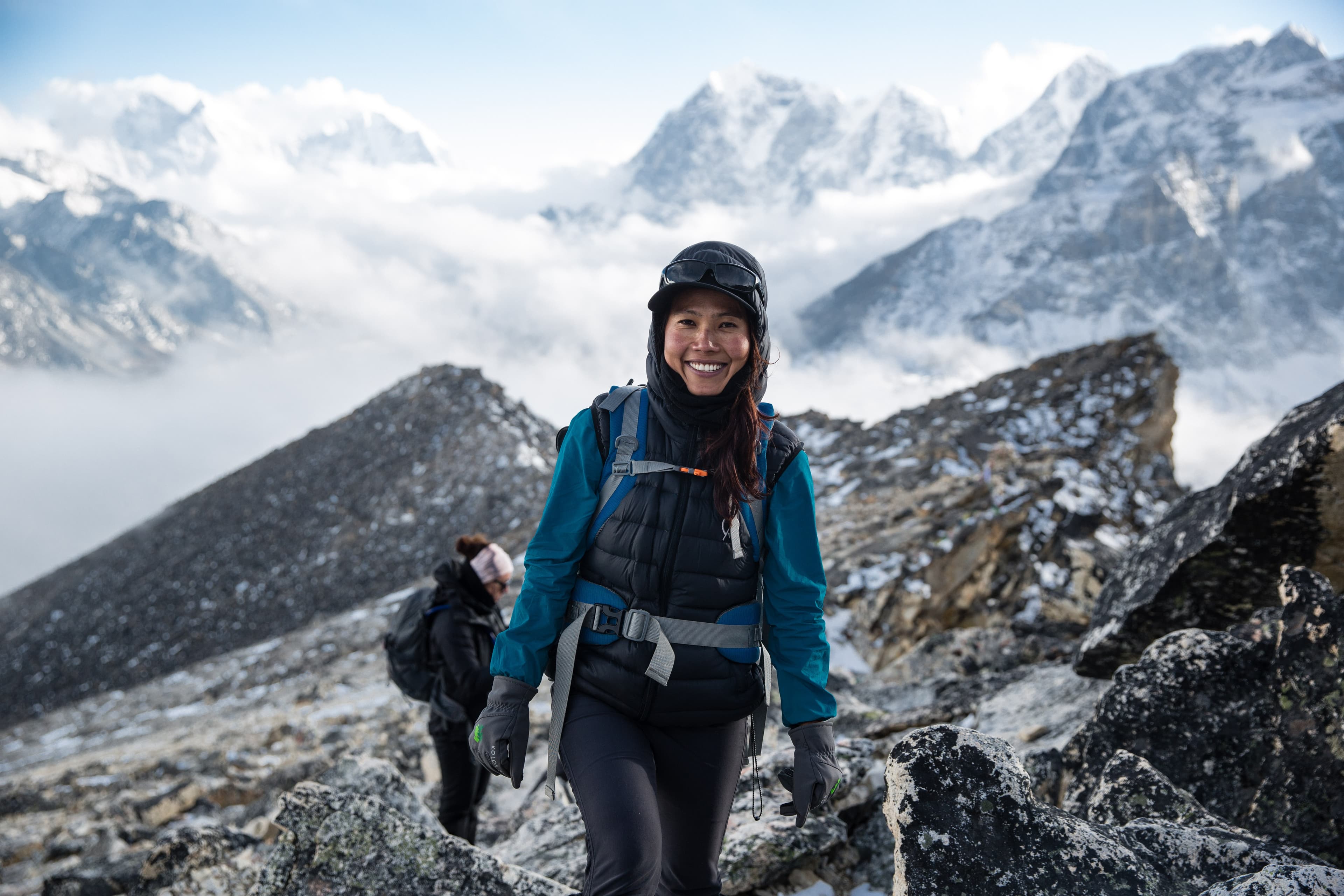 A hiker celebrating on a rock in front of snowy mountains